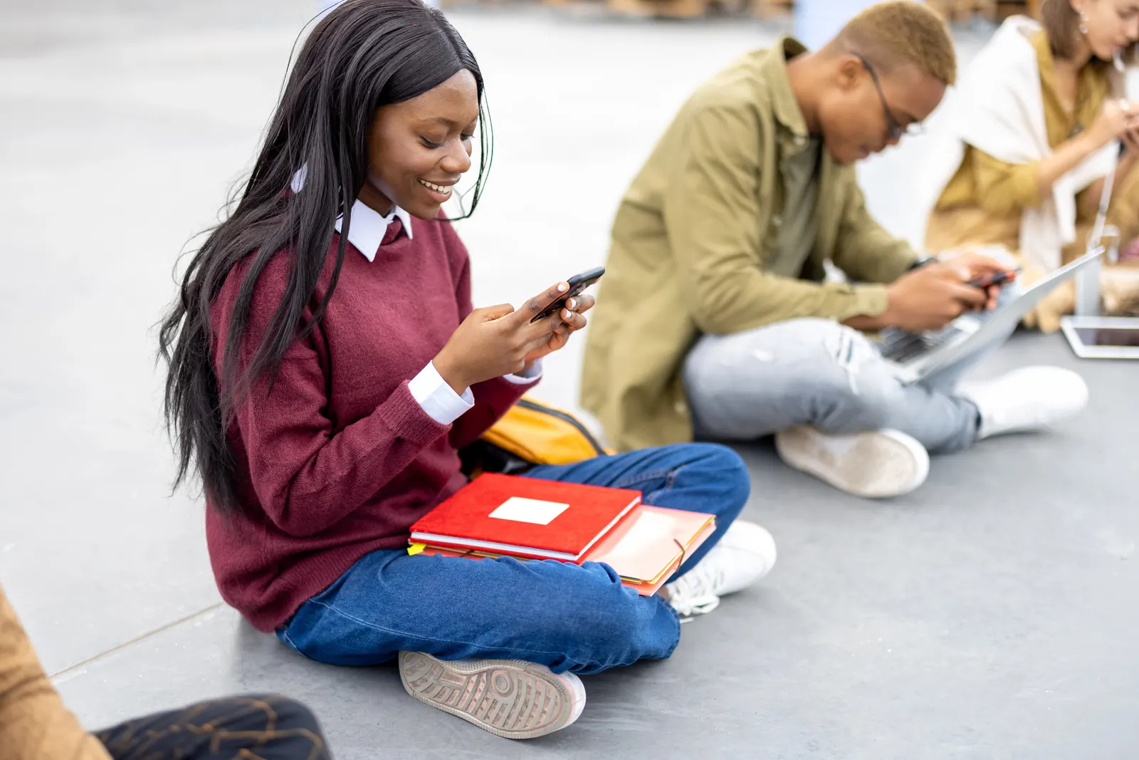 Étudiante qui révise sur son téléphone, ses livres à côté d’elle